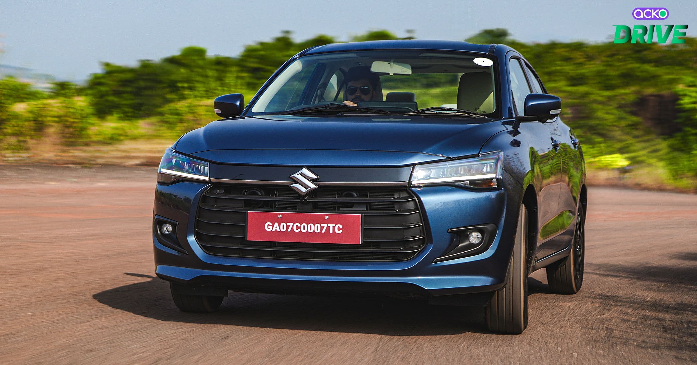 A dark blue Suzuki car driving along a road with a blurred green background.