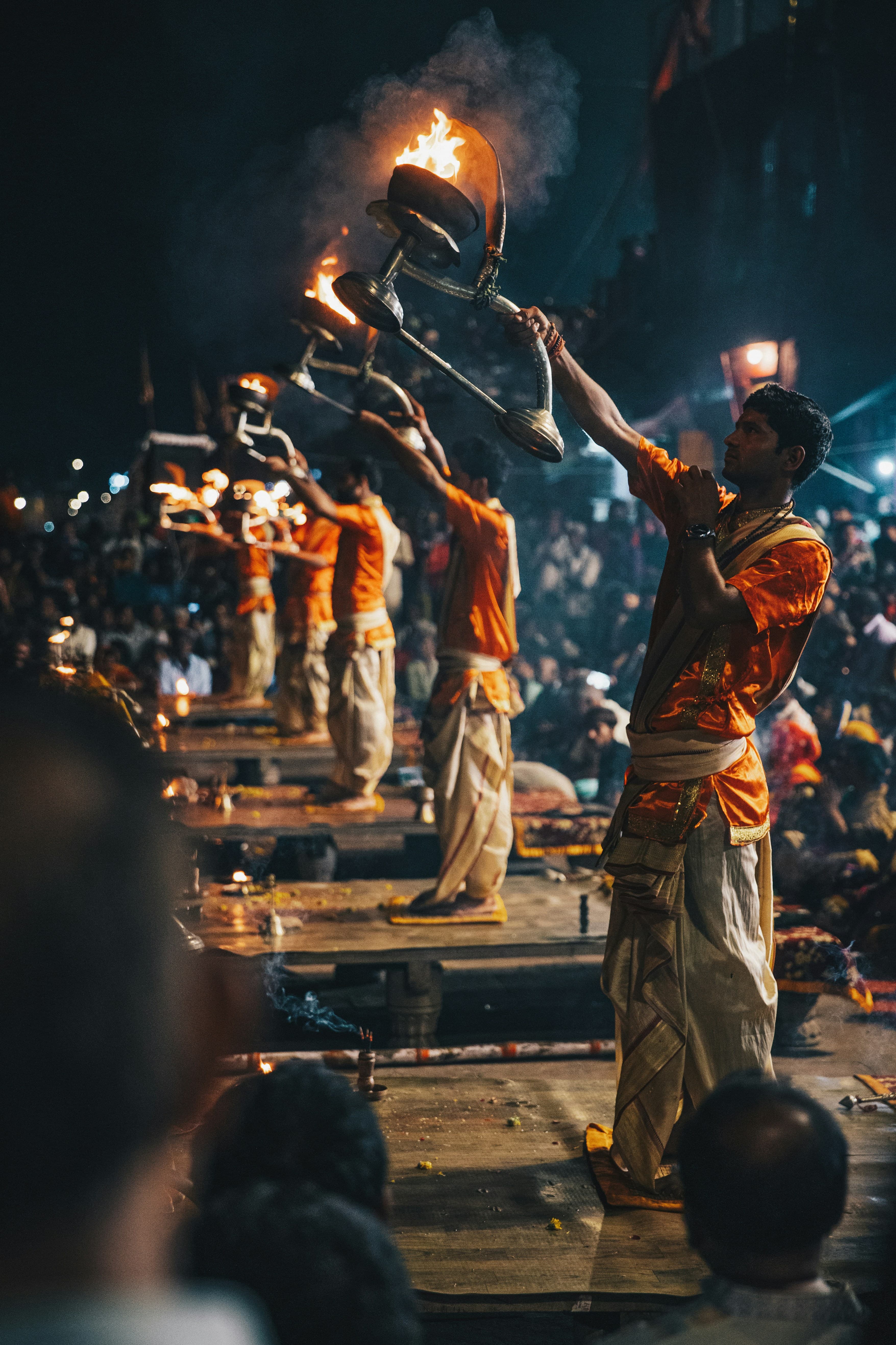 Hindu priests perform the Ganga Aarti ritual with large flaming brass lamps at night.