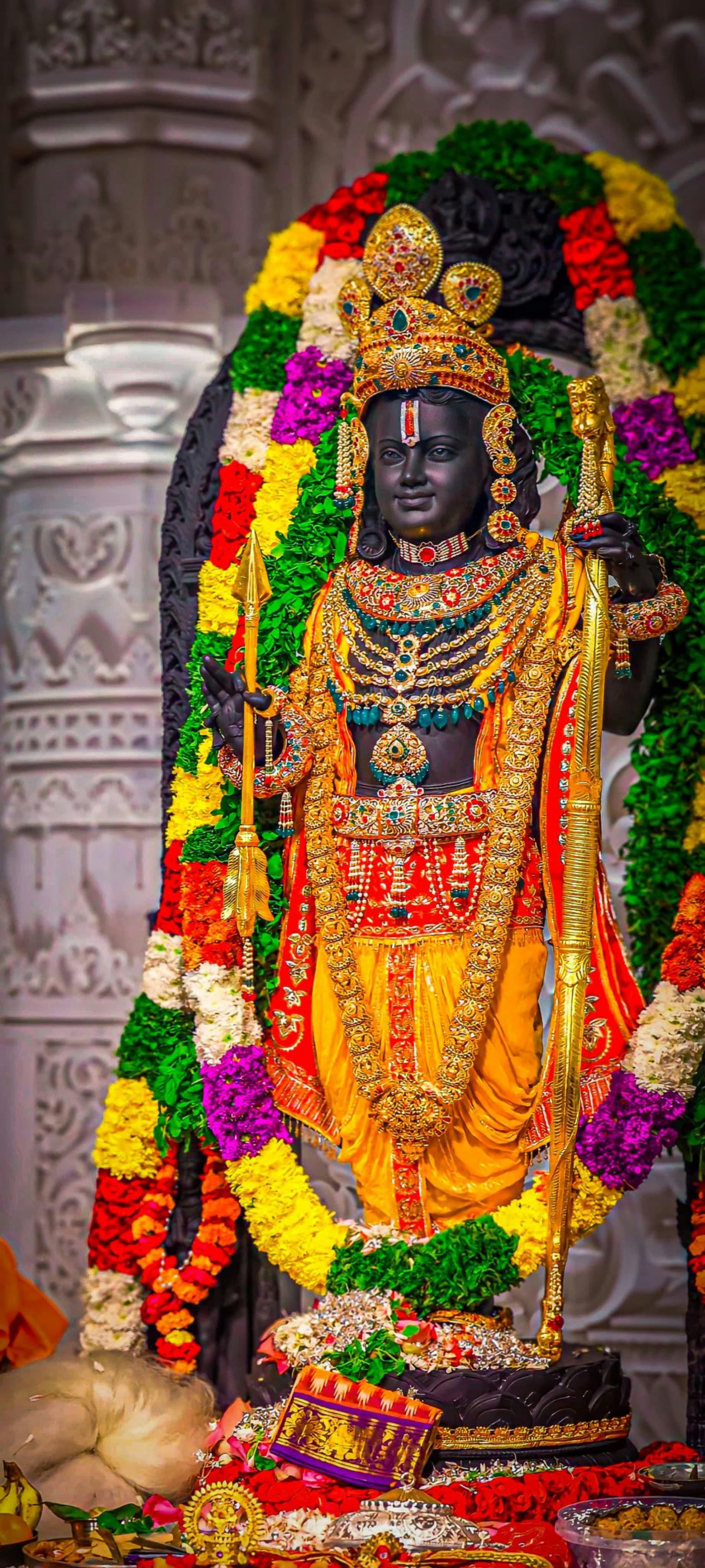 Ornate black statue of Lord Rama holding a golden bow, adorned with floral garlands.